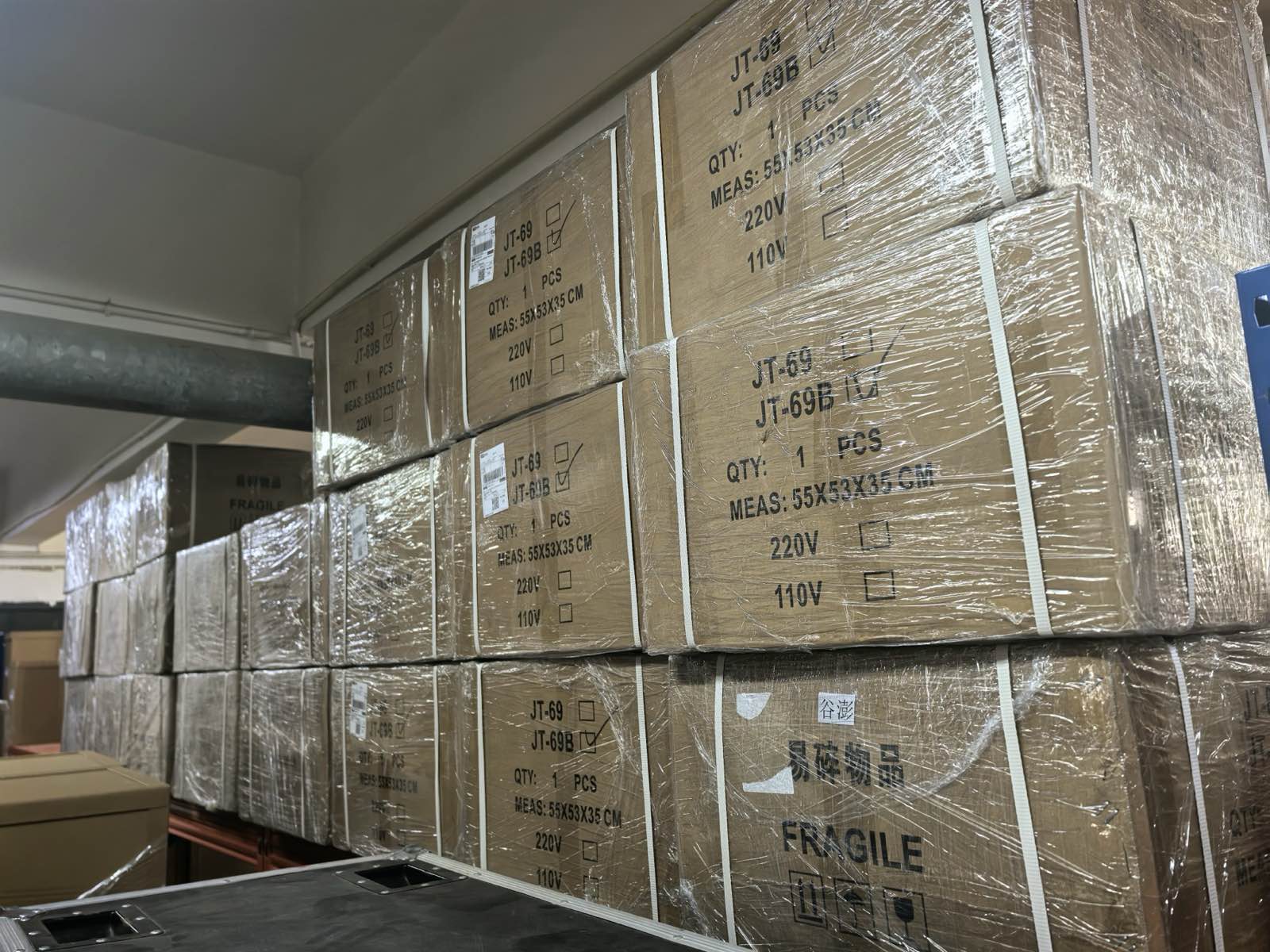 Stacked export cartons wrapped in film, each marked with model number and voltage